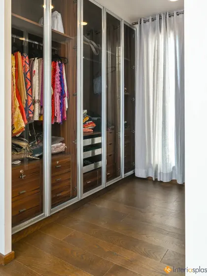 A look inside a well-organized walk-in closet. The combination of hanging space, drawers, and shelves, all behind clear glass doors, makes it easy to see and access your entire wardrobe.