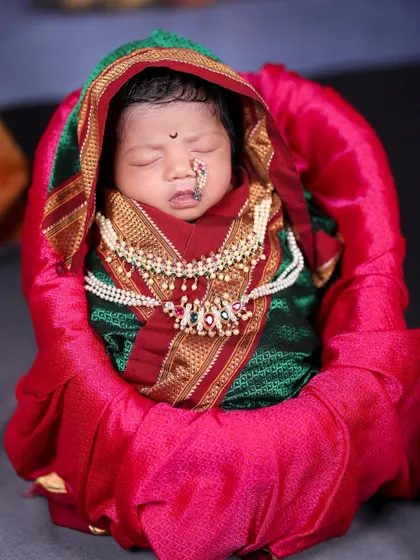 A close-up of a newborn baby girl dressed in a traditional Marathi nauvari saree wrap, complete with a tiny nose ring. It’s a beautiful way to honor our culture from the very beginning.