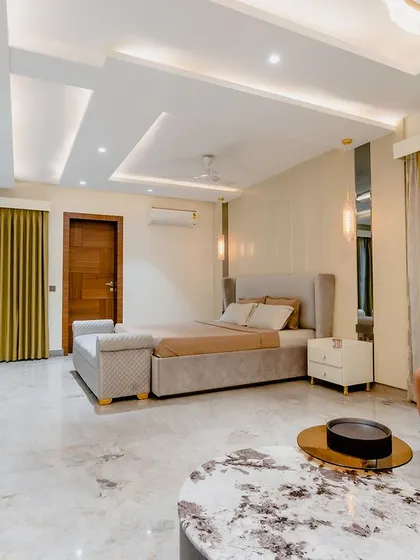 This spacious master bedroom is the definition of understated luxury. The neutral tones are punctuated by a rust-colored armchair, and the large windows flood the room with light.