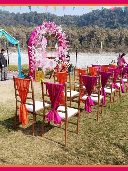 Guest seating at a riverside Mehendi, with chairs decorated in bright pink and orange drapes, overlooking a beautiful natural view.