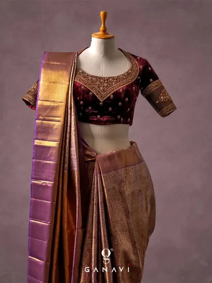 A luxurious deep maroon velvet blouse paired with a shimmering purple and gold Kanjeevaram saree. The V-neck blouse is adorned with delicate floral embroidery, adding a touch of regal softness to the rich fabric.
