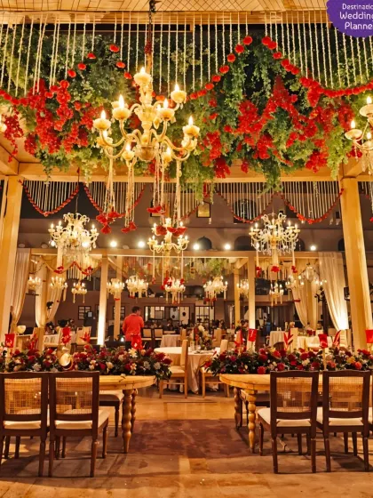 A grand and opulent wedding setup with a ceiling of red flowers and greenery, complemented by magnificent crystal chandeliers for a truly regal feel.