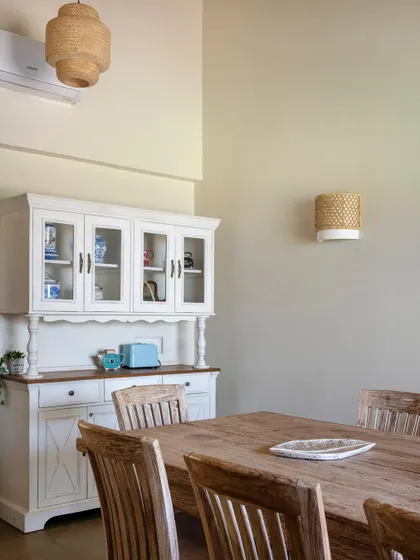 The dining area features a large wooden table and a classic white hutch, perfect for family meals. Wicker pendant lights add to the natural, earthy aesthetic.
