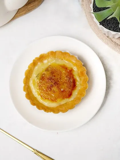 A top-down flatlay of the crème brûlée tart with a decorative golden spoon. This styled shot adds a touch of elegance, suitable for social media or a premium menu.