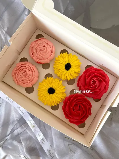 A box of six assorted floral cupcakes, featuring vibrant red roses, cheerful sunflowers, and delicate pink peonies. A perfect gift box for any occasion.