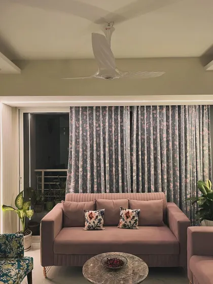 This living room setup combines a comfortable dusty rose sofa with elegant, floor-to-ceiling curtains and carefully placed plants to create a space that feels balanced, serene, and stylish. The marble coffee table adds a touch of modern luxury.