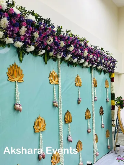 A serene and elegant backdrop for a baby shower. The light blue fabric is adorned with golden lotus cutouts and delicate jasmine flower hangings, creating a peaceful and sophisticated ambiance.