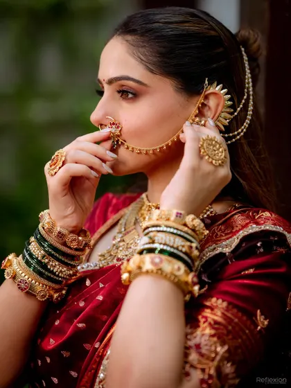 This profile shot highlights the intricate details of the Maharashtrian bridal look, from the nath to the layered earchain. The makeup is kept soft to balance the grandeur of the accessories.