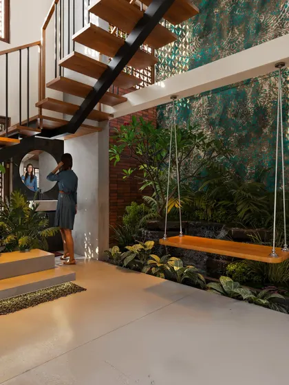 An indoor courtyard featuring a wooden swing suspended over a green space with a small waterfall. The design includes a floating staircase and a textured accent wall.