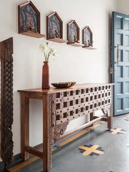 This gorgeous teak console, likely repurposed from an old door, is a conversation starter in the foyer. Above it, custom-made shelves house antique brass sculptures of musicians, adding to the home's authentic, vintage charm.