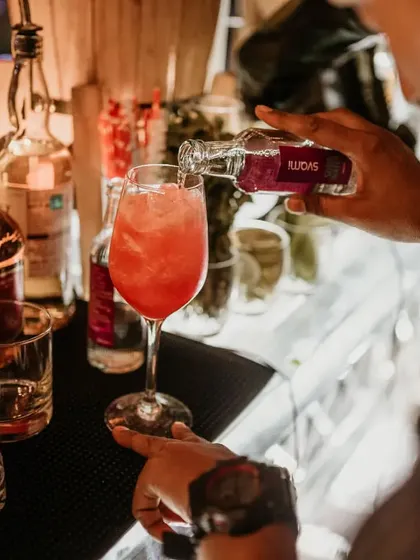 A close up of a cocktail being crafted. Our mixologist adds a final touch to a vibrant red drink, showcasing the care that goes into every single order.