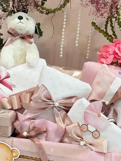 A detail shot of the pink baby hamper, showing the delicate pearl-adorned ribbons, a tiny jewelry box, and other sweet, feminine touches that make this gift so special.