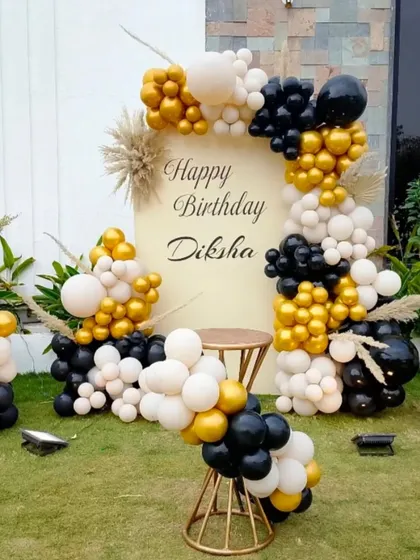 An outdoor birthday setup with a modern, minimalist feel. The black, white, and gold balloon garland beautifully frames the custom backdrop.