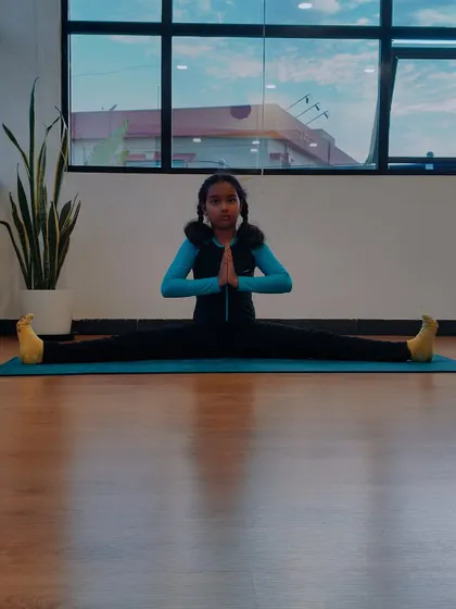 Charvi in a seated wide-legged forward bend with hands in prayer. Her focus and dedication are evident in every pose she practices.