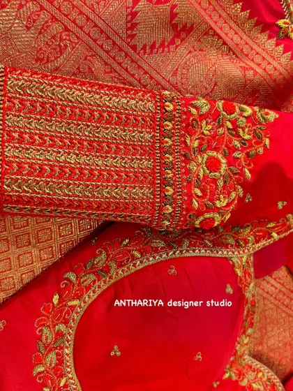A close-up of a red blouse sleeve with dense, traditional gold embroidery.