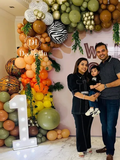 A family portrait in front of a massive balloon arch with animal-print details and a large marquee '1'.