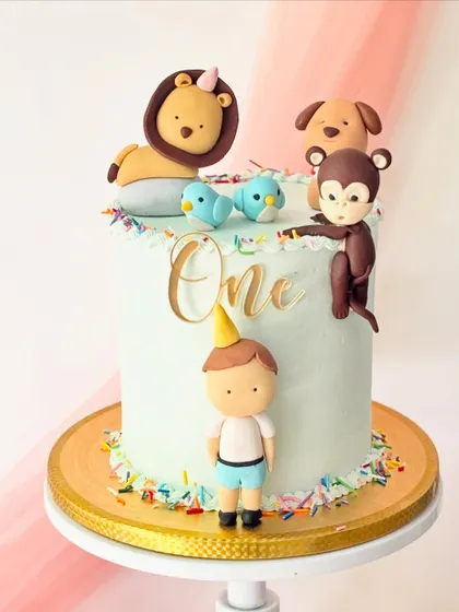 A sweet first birthday cake with a boy and his animal friends. The cake is topped with a lion, dog, and monkey, all handcrafted from fondant.