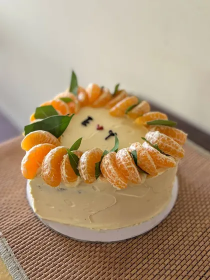A rustic and minimal heart-shaped cake. It's decorated with a crown of fresh mandarin orange slices and leaves, with simple initials in the center for a personal touch.