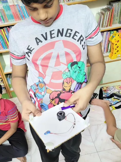 A student proudly holds up the electric bell he wired himself. These projects demystify technology and empower kids to see themselves as creators.