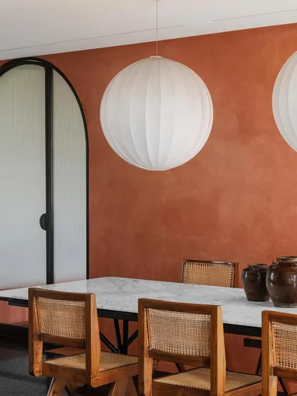 A closer look at the dining area, where large spherical fabric lights float above the marble table. The warm terracotta wall and cane chairs create a welcoming environment for gathering.