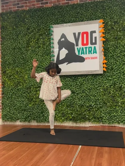 A young girl holds a steady Vrikshasana (Tree Pose), finding her balance and calm.