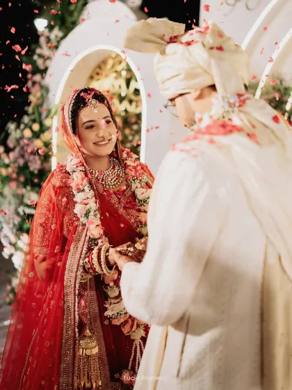 The bride's smiling face as she and the groom exchange garlands, surrounded by falling petals.