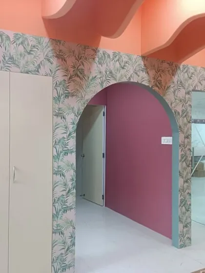 A green palm leaf wallpaper adds a fresh, tropical vibe to this space, beautifully complementing the arched doorway and pink walls. This shows how wallpaper can connect different areas of a home.