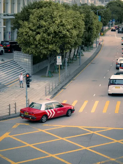 A high-angle shot of a classic red Hong Kong taxi. The graphic yellow lines on the road create a strong compositional element in this urban scene.