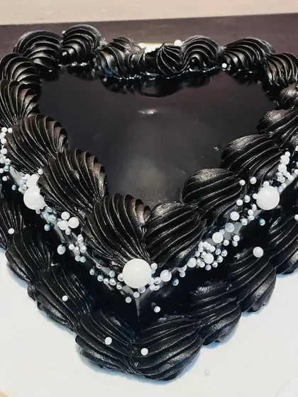 A striking all-black vintage-style heart cake. This Belgian chocolate cake is decorated with intricate black piping and delicate pearl sprinkles for a touch of gothic elegance.