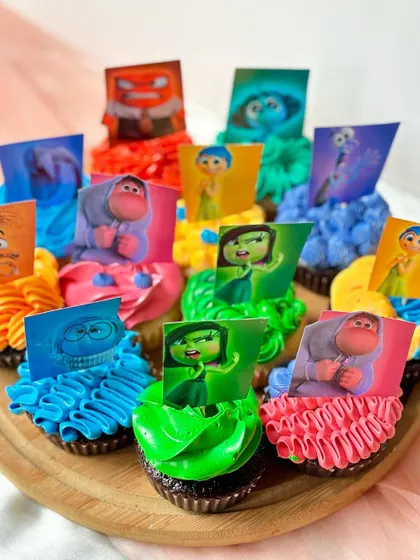 The same 'Inside Out' cupcakes, shown here with the addition of printed edible character toppers. This demonstrates an alternative way to enhance a theme, combining colourful buttercream with specific character art.