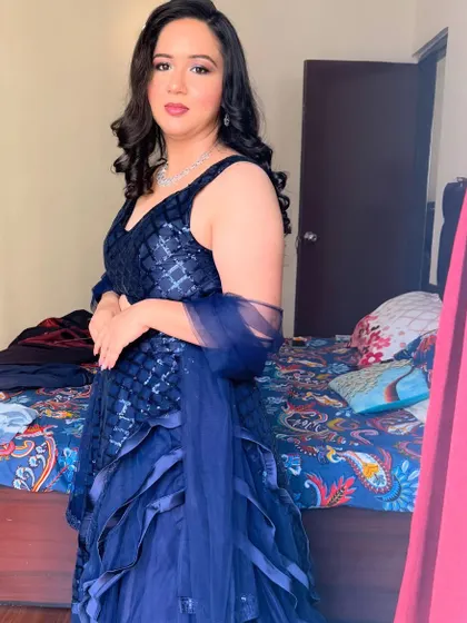 A client ready for a party in a beautiful navy blue gown. The makeup is soft and elegant, with loose curls framing her face.