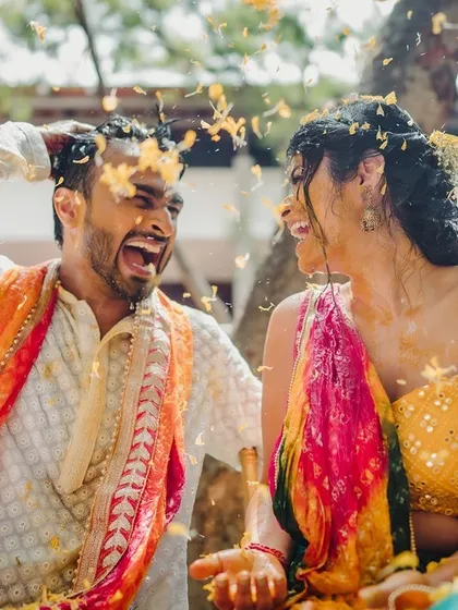 A couple shares a huge laugh as they are showered with petals during their outdoor Haldi celebration.