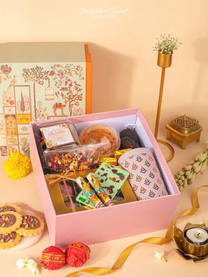 A soft, feminine Diwali hamper in a pink box, filled with cookies, chocolates, and other treats, styled with traditional elements.