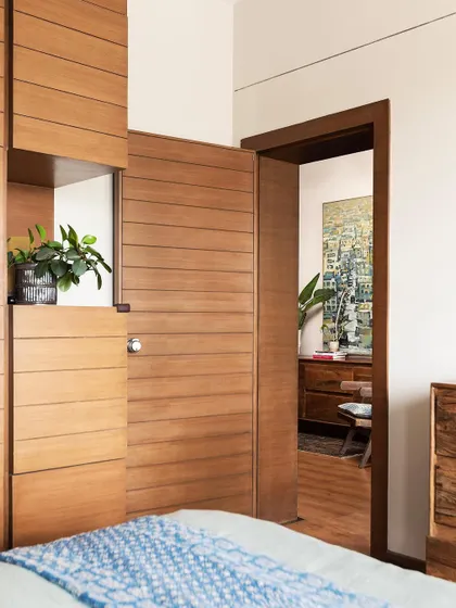 A view from the bedroom into the main living area of 'Reweave Stories'. The consistent use of wood for the flooring and door frames creates a warm and cohesive feel throughout the home.