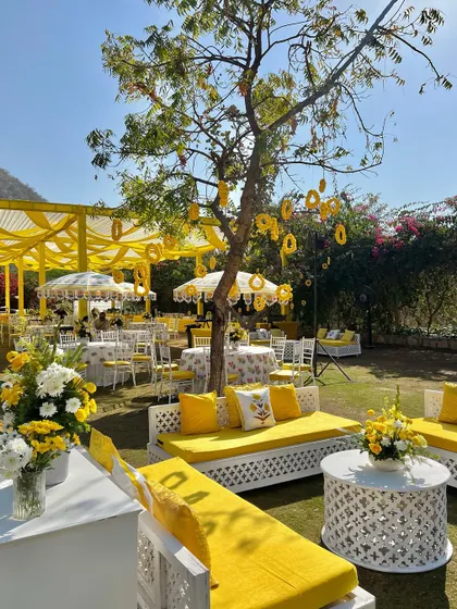 White latticework seating with bright yellow cushions creates a fresh and modern look for this sunny outdoor haldi celebration.
