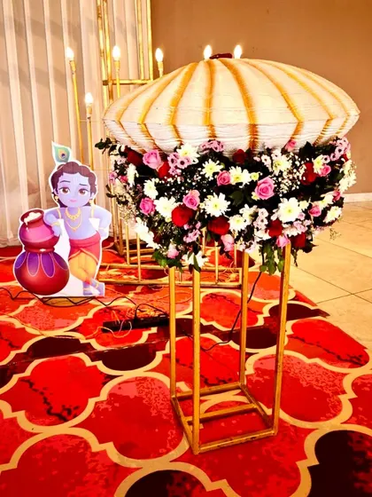 A detail from the naming ceremony, showing a Little Krishna cutout next to a beautiful floral arrangement on a golden stand.