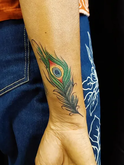 A close-up of a colorful peacock feather tattoo on the wrist. The intricate lines and blend of colors make feather designs a beautiful and effective option for covering small, unwanted tattoos.