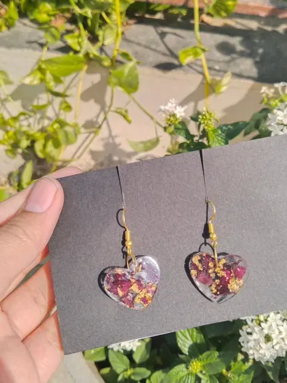 A close-up of my preserved rose petal earrings. These heart-shaped resin earrings are filled with real rose petals and flecks of gold foil, making them a romantic and delicate accessory. They are a great way to preserve a single special flower.