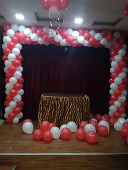 A spiral red and white balloon arch on a stage, creating a focal point for a cake-cutting ceremony or performance area.