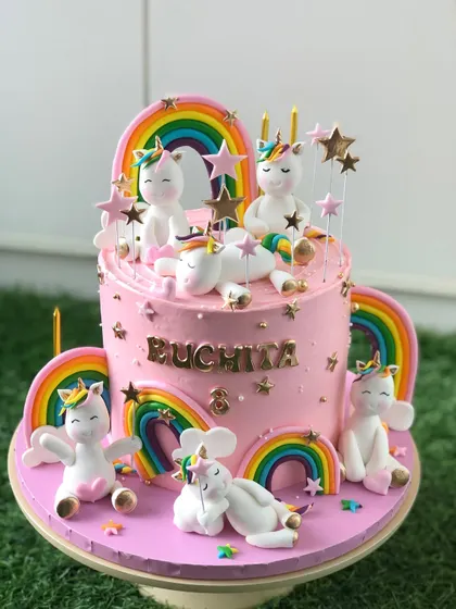 A truly magical unicorn cake, covered in pink buttercream and adorned with a whole family of cute, playful unicorns and rainbows.