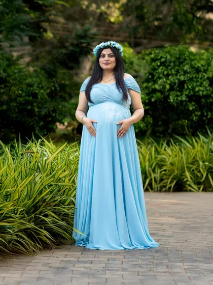 A beautiful solo portrait of a mom-to-be wearing a floral crown and a light blue gown. The lush green background makes the colors pop.