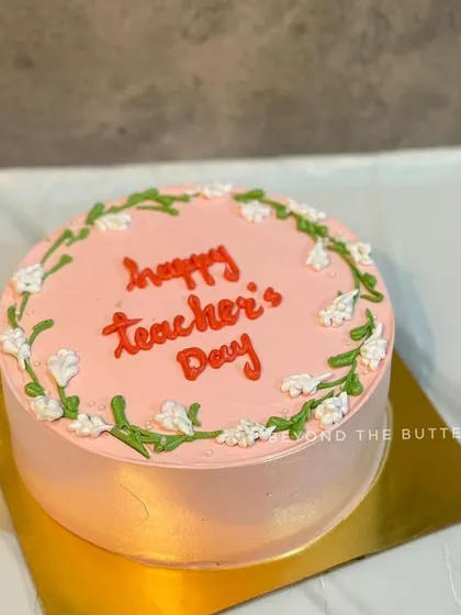 A lovely pink Teacher's Day cake with a delicate white floral vine design.
