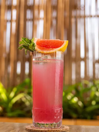 A tall pink grapefruit mocktail, shot against a natural bamboo background for a tropical, relaxed feel.