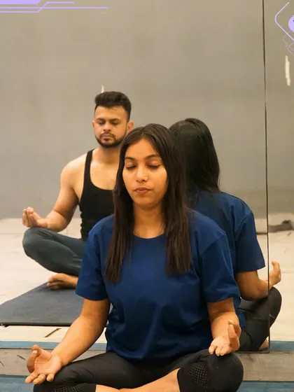 Two members practicing a seated meditation pose in front of a mirror. The reflection adds a beautiful dimension, symbolizing the inner reflection that yoga encourages.