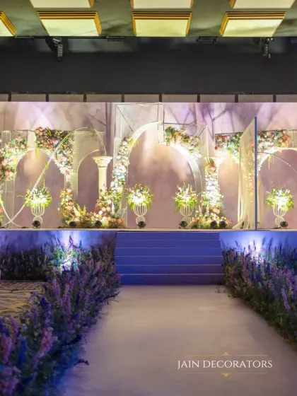 A stage designed to feel like a portal to a fairytale. A lavender-hued pathway leads to a series of ethereal arches adorned with pastel flowers, creating a dreamy and romantic setting for the couple.