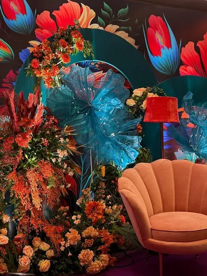 Another angle of the Bhaat ceremony decor, highlighting the mix of textures from the floral arrangements, the soft armchair, and the artistic backdrop. The lighting enhances the vibrant colors, making the space feel alive.