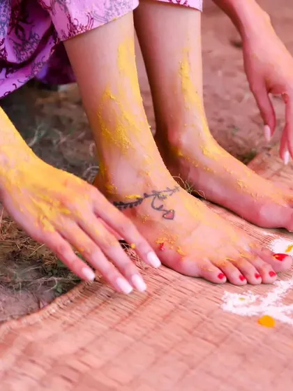The beautiful details of the Haldi ceremony. This shot focuses on the bride's feet and hands, adorned with turmeric, and the traditional rangoli design on the mat.