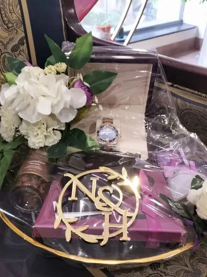 A closer look at a luxury gift platter, centered around a boxed watch. The arrangement includes other personal items and is finished with a custom monogram and silk flowers, showcasing our detailed packing service.