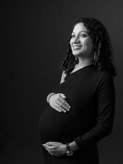 A classic black and white maternity portrait against a dark background. The lighting is carefully shaped to highlight the mother's features and her beautiful pregnancy glow.