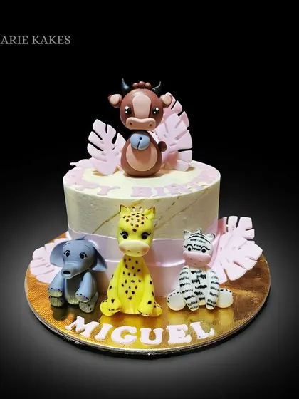 A sweet safari-themed cake for Miguel. This design includes a buttercream finish and is decorated with hand-sculpted baby animals like a cow, elephant, giraffe, and zebra.